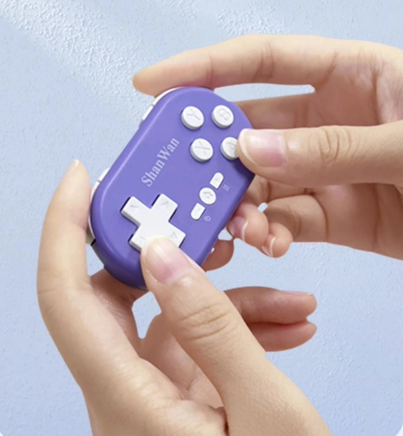 Hand holding a purple handheld gaming console with text on a light blue background