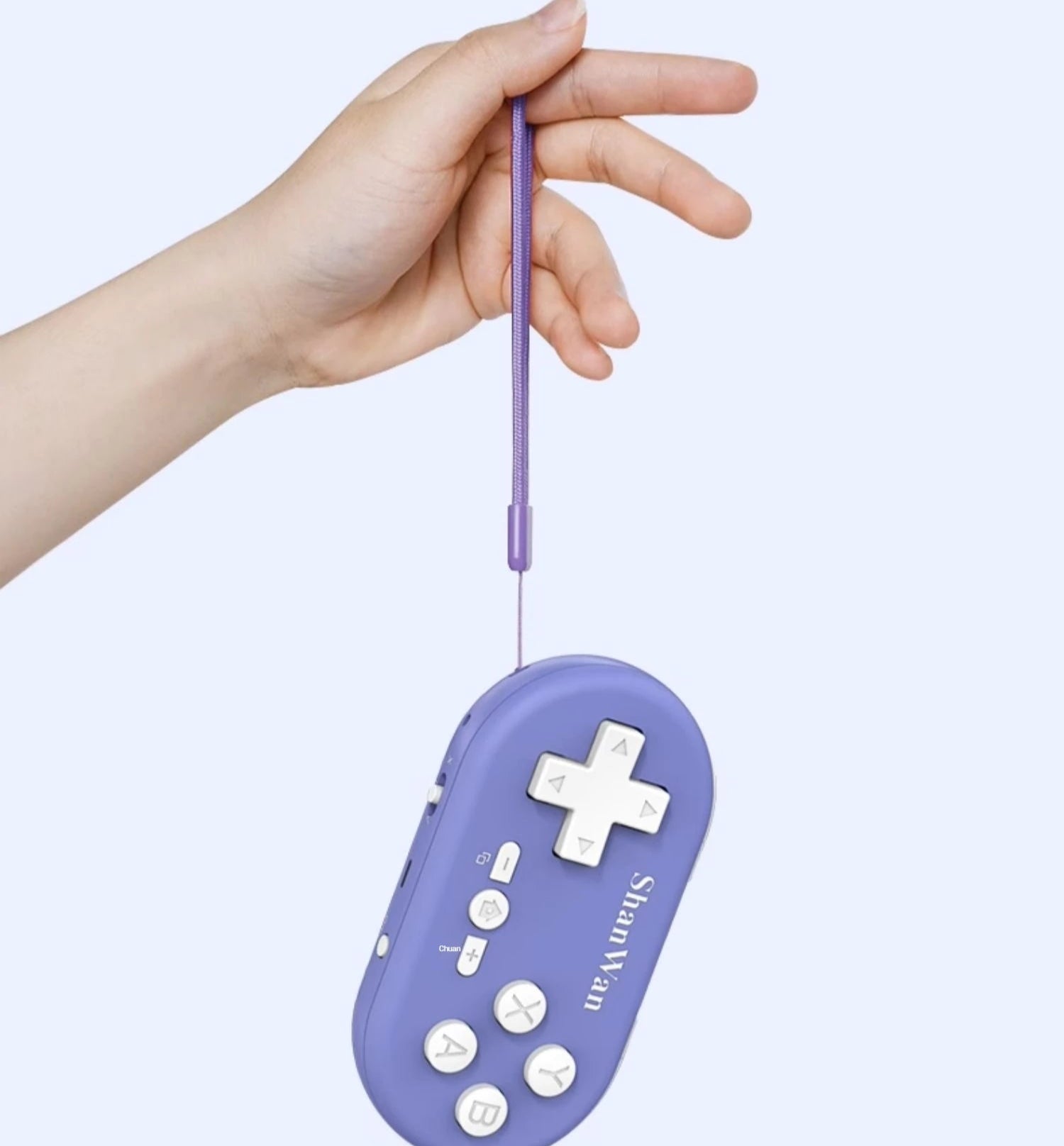 Purple handheld gaming console with a lanyard, held by a hand against a light purple background.